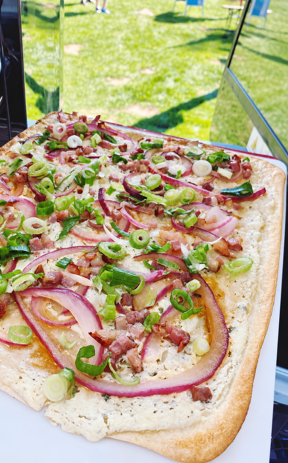 Frisch belegter Flammkuchen mit Speck, roten Zwiebeln und Frühlingszwiebeln